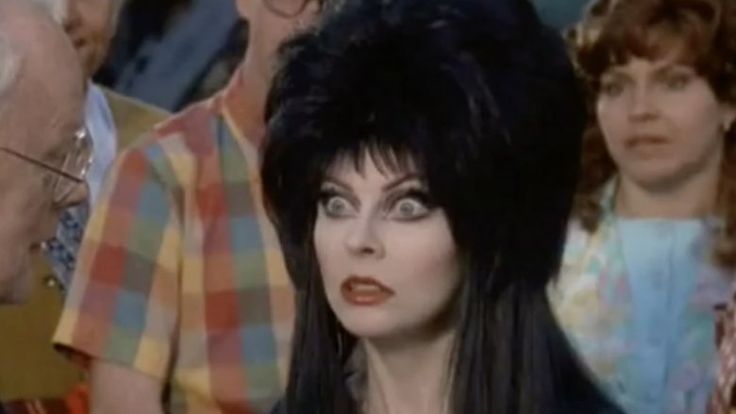 a closeup portrait of a woman with dark, gothic styled hair staring directly at the camera. the woman is dressed in a darkcolored dress.