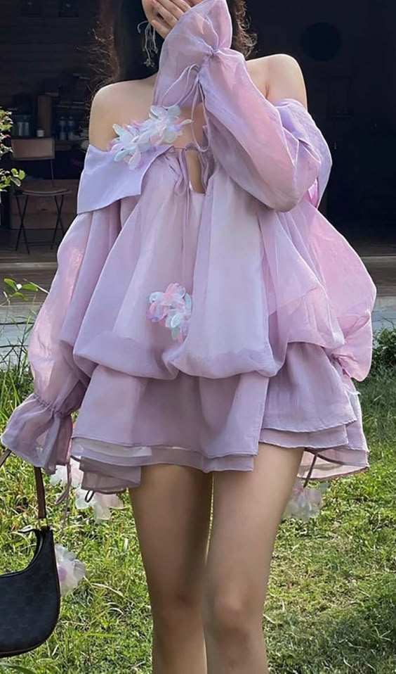 a young woman is standing in a field of green grass, wearing a beautiful lavender dress with floral embellishments. the dress is made of a soft, flowing fabric that gives it a dreamy and ethereal look.  she's looking down, her face partially obscured by her hand.  her hair is down and flowing freely. the overall image is very feminine and delicate.
