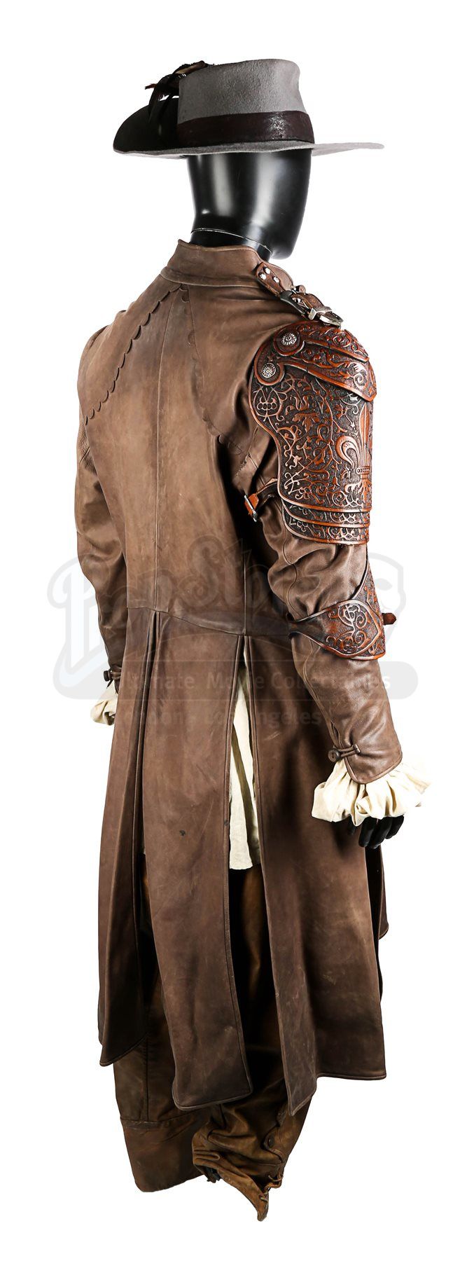 a brown leather costume, consisting of a hat, coat, and pants, is displayed on a mannequin. the hat is a light gray color with a dark brown band, and the coat is a long brown leather jacket with an ornate leather epaulette on the right shoulder. the pants are also brown leather and appear to be baggy. the mannequin is black.