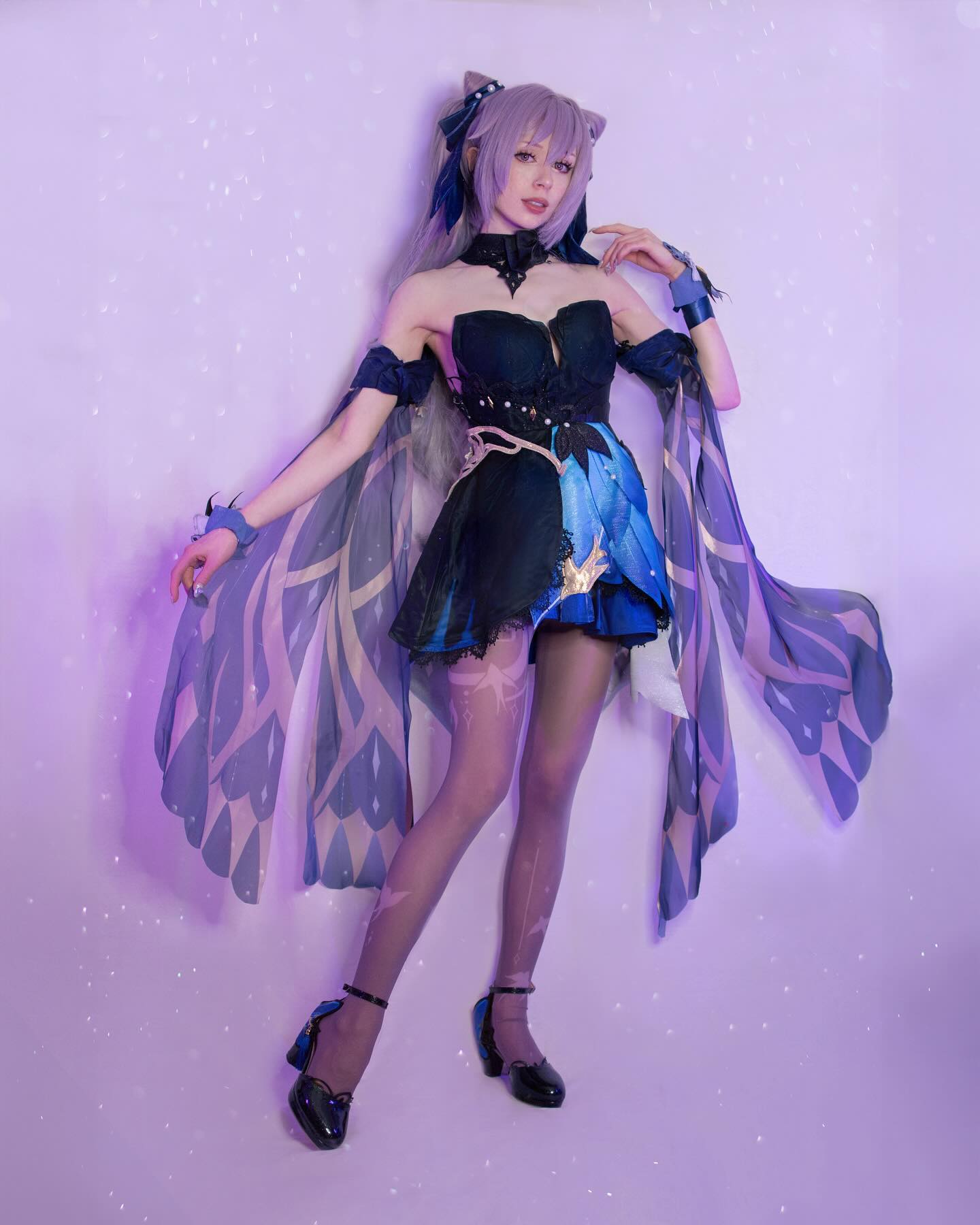 a fulllength shot of a young woman cosplaying as a character, possibly raiden shogun from genshin impact,  posing against a purple background with light speckles. the cosplay includes a detailed dark blue and purple dress with winglike extensions, intricate detailing, and black heels. the cosplayer's makeup and wig are styled to match the character. the overall feel is ethereal and elegant.