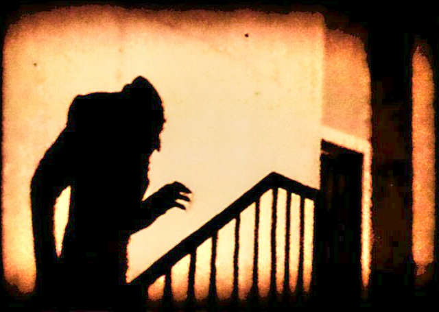 a shadowy figure resembling a monstrous vampire ascends a flight of stairs. the setting is dark and mysterious, illuminated by a warm, lowkey light source. the image evokes a sense of horror and suspense.