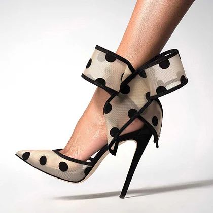 a closeup shot of a woman's foot wearing a pair of black and white polka dot high heels with a bow on the ankle. the shoes are elegant and stylish, perfect for a special occasion. the background is a simple white surface, allowing the shoes to stand out.