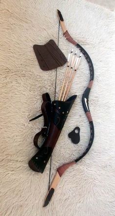 this is an image of an archery set, complete with a recurve bow, a set of arrows, and a leather quiver. the bow is crafted from wood and possesses a classic recurve design, its limbs elegantly curving away from the archer. the arrows, fletched with feathers for stability, are neatly housed within the quiver, which itself is made from richlytoned leather and features decorative tooling. this arrangement suggests a focus on traditional archery, highlighting the craftsmanship inherent in these tools.