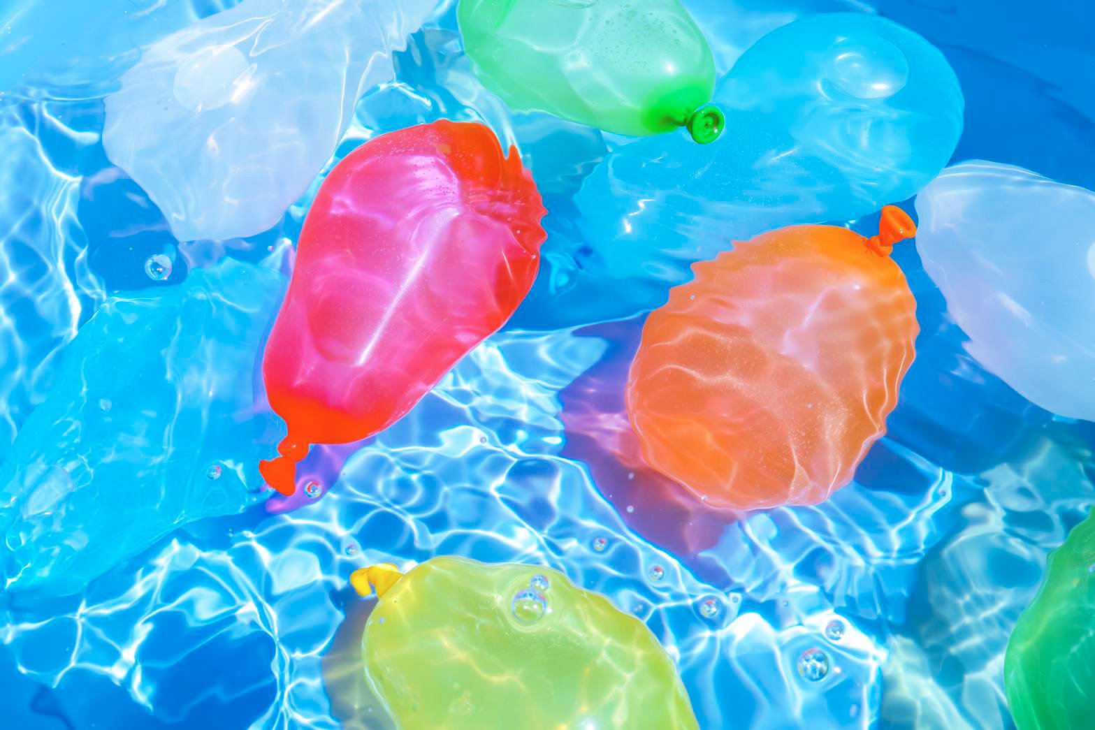 this is an image of colorful water balloons floating in a pool.  the water is bright blue and the balloons are translucent.