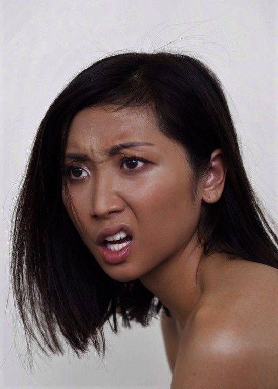 closeup portrait of a young asian woman with dark hair cut into a bob. her expression is one of intense disgust or annoyance; her brow is furrowed, her mouth is open in a grimace, and her eyes are narrowed.  she appears frustrated or angry. the background is plain white.  the image is a studio shot, focusing on the woman's face and upper shoulders. her skin tone is medium brown, and her shoulders are bare.