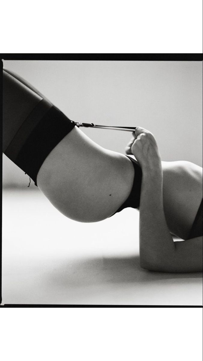the black and white photograph depicts a woman's body from the waist down, lying on her side.  she's wearing black stockings and a darkcolored lingerie top or bottom, partially visible. a garter belt or strap is noticeable across her thigh and stomach. the image is artistically lit, emphasizing curves and shadows, creating a sensual and intimate atmosphere.  the focus is on the woman's body and the interplay of light and shadow. the style is minimalist and suggestive.