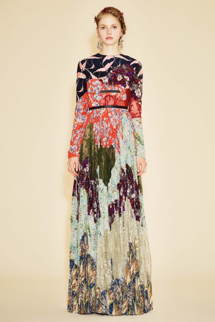 a woman is wearing a colorful floral dress, the dress is pleated and has long sleeves. the woman is standing in front of a white background, posing for the camera.