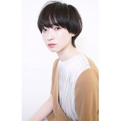 a woman with short, black hair and bangs is looking at the camera. she is wearing a beige and white tshirt. the background is white.