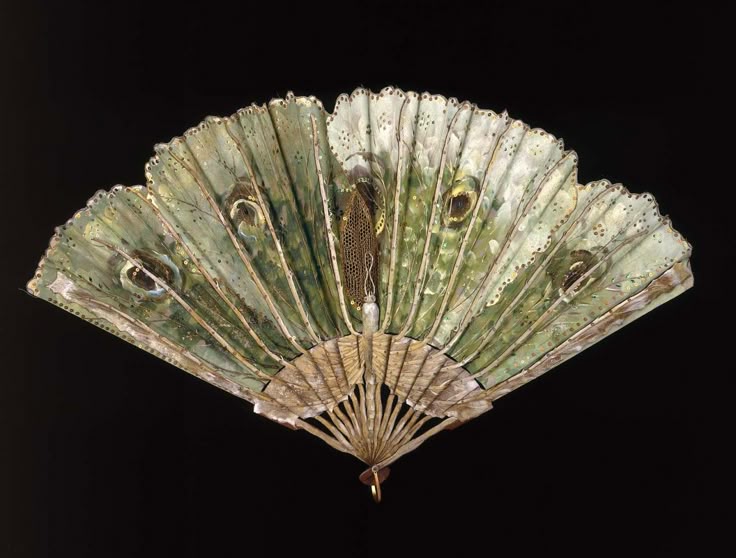 an antique fan with a design featuring peacock feathers, primarily green and gold in color. the fan is partially open, showcasing its intricate detailing and ornate construction. the background is a solid black.