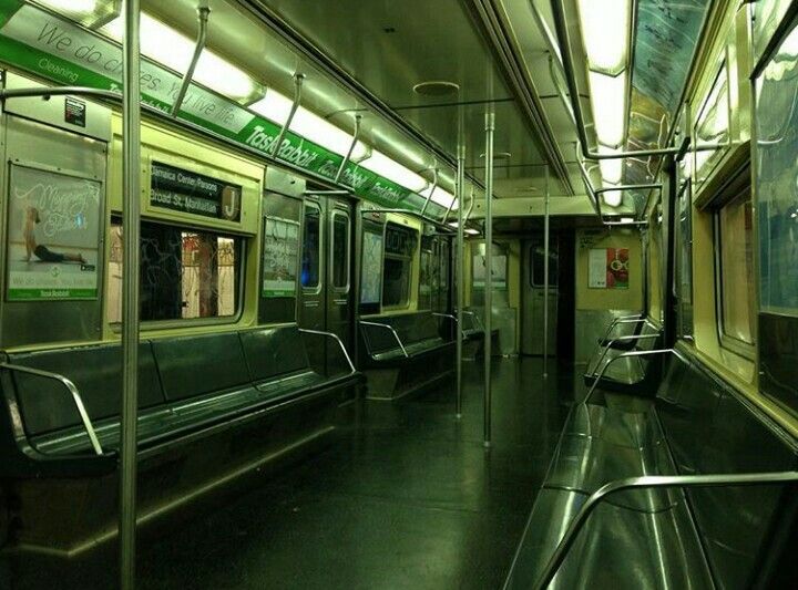 the image shows the interior of an empty new york city subway car. the seats are dark green, and the overall lighting is muted green, creating a dark and moody atmosphere.  green advertisements for taskrabbit and a cleaning service are visible along the walls.  the train appears to be a j train, as indicated by signage. the overall feel is one of stillness and quiet.