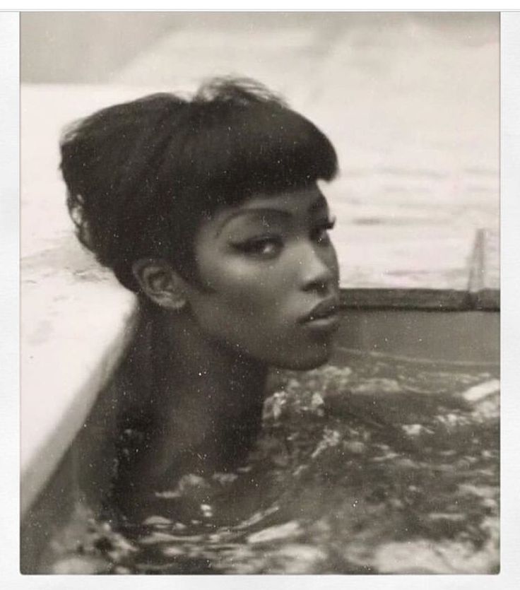 a black and white portrait of a woman with dark hair and striking eyes, posed in a bath tub. her hair is slicked back and wet, and she is looking directly at the camera with a sultry expression. the image has a retro, vintage feel and captures the woman's beauty and mysterious nature.