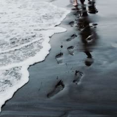 a photo of a black sand beach with crashing waves. the white ocean water is juxtaposed with the dark sand and creates a stark contrast. the image also shows footprints in the wet sand, suggesting that someone has walked on the beach. the photo is a good example of how nature can be both beautiful and dramatic.