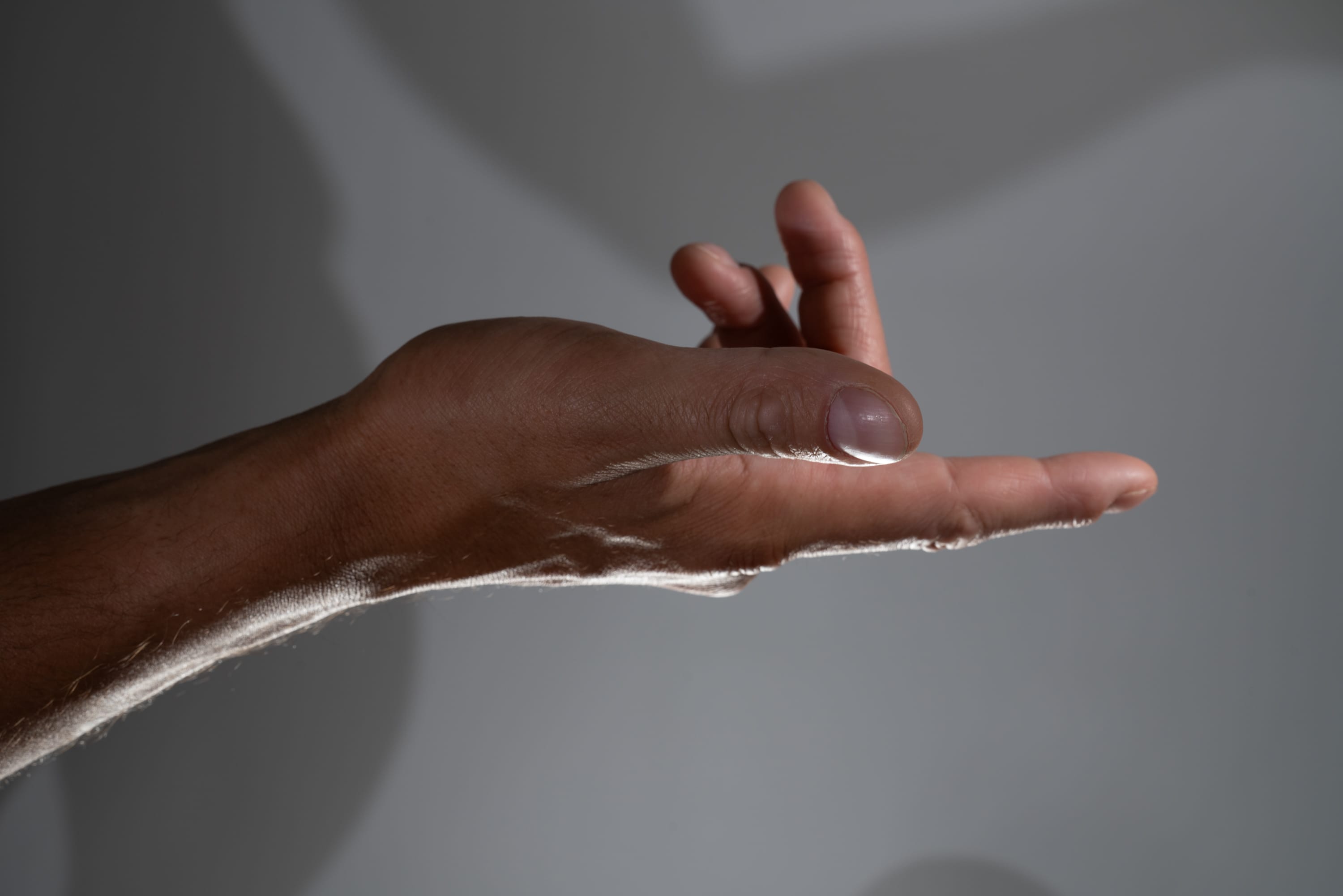 a black man's hand is outstretched against a gray background. the hand is illuminated with soft light, creating shadows on the background.