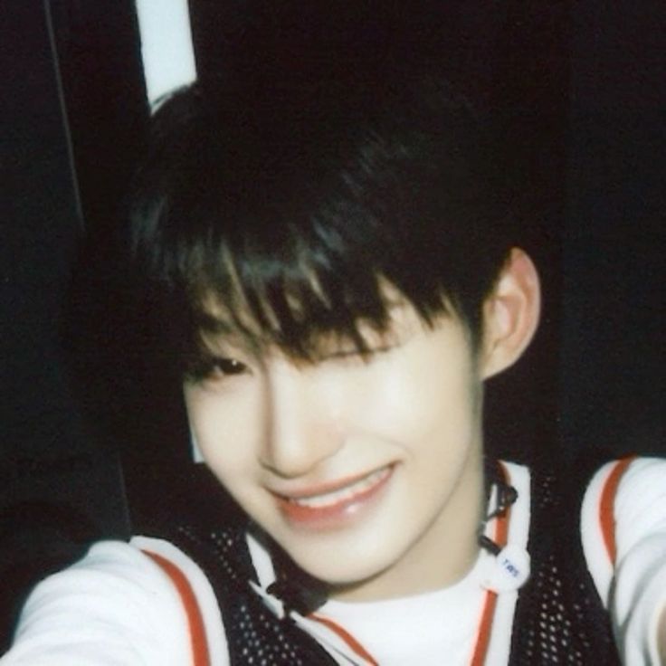 a closeup shot of a young man smiling happily. he has black hair and is wearing a white shirt and a black and red vest. the photo is taken with a vintage camera and has a blurry effect.