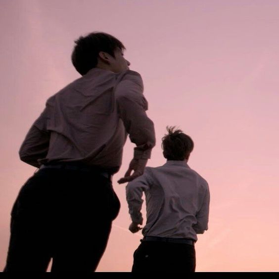 he image shows two young men running towards the horizon against a soft, pinkishpurple sunset sky. the perspective is from a low angle, looking up at the men, emphasizing their movement and the vastness of the sky. the lighting is natural and warm, casting the men in silhouette. the overall mood is one of freedom and youthful energy.