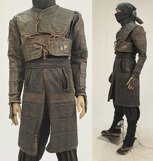 this image shows a  ninja warrior. he is wearing dark leathery armor with a black ninja mask. the armor includes a chest plate, shoulder pads and arm guards, with a decorative fabric covering his arms and torso. the warrior is wearing loose fitting pants.