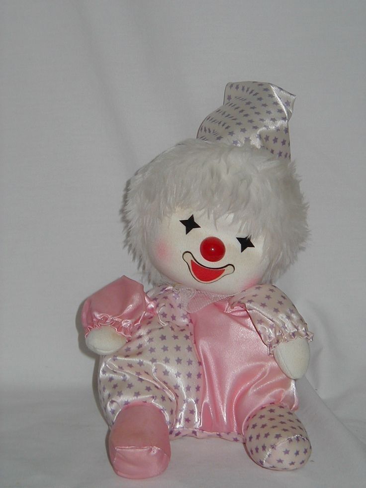 a closeup shot of a pink and white plush clown doll sitting on a white surface. the clown has a white face with a red nose, black eyes, and a big smile. the doll is wearing a pink and white star patterned outfit and a purple and white star patterned hat.
