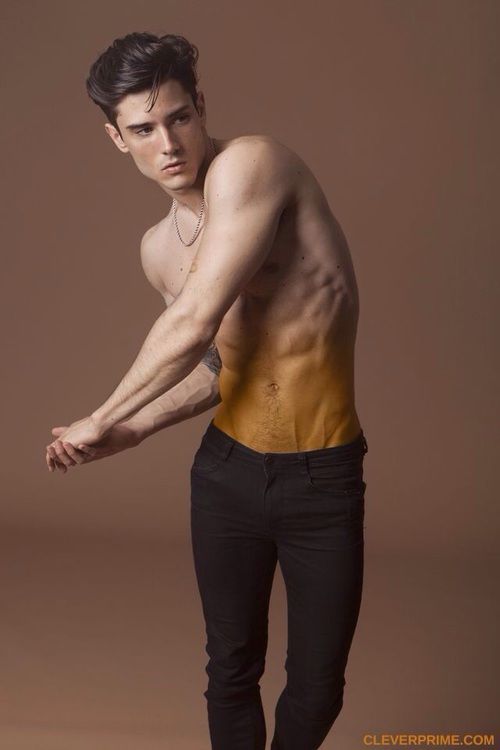 a shirtless man with a muscular physique poses in a studio. he is wearing black jeans and has a six pack. the man is looking at the camera. he is handsome and attractive.
