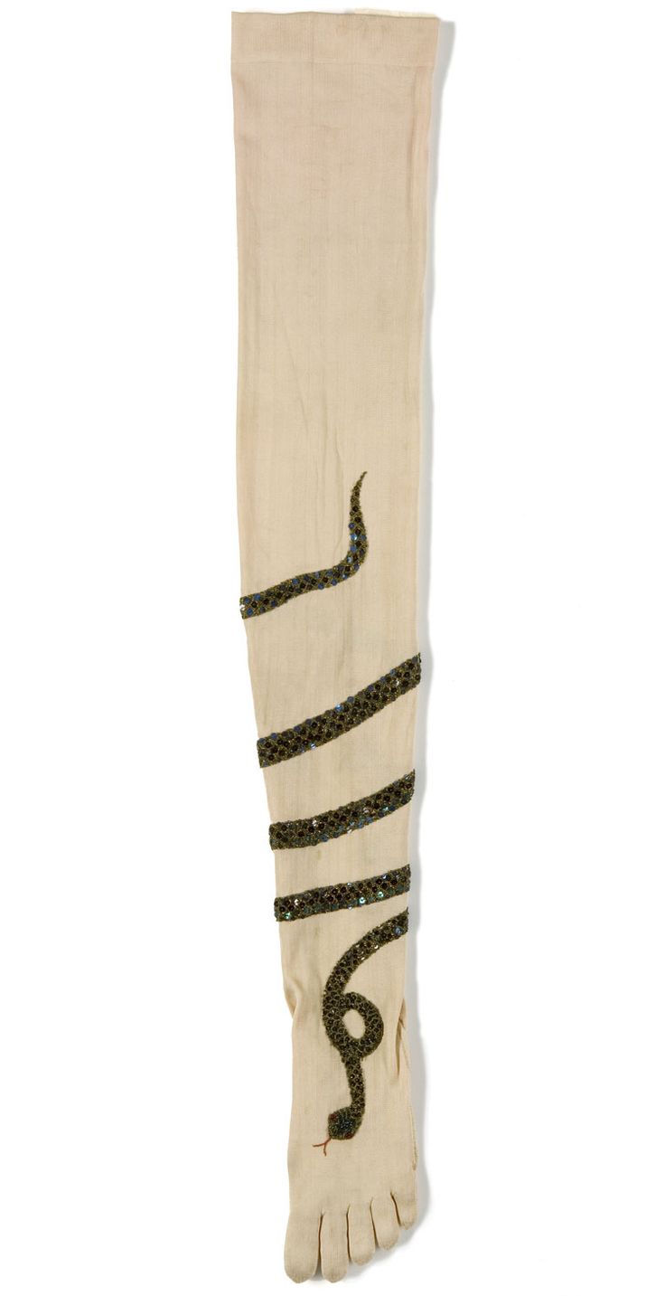 a beige beaded glove featuring a snake pattern. the glove is long, reaching above the wrist, and has individual fingers with visible seams. the snake design is made of dark beads or sequins that wrap around the glove. the snake's head is visible near the bottom of the glove, and the body extends up the glove in a winding pattern. the beads or sequins appear to be densely packed, creating a textured surface.