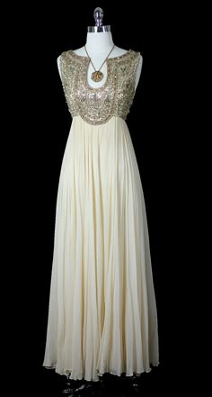 a white sleeveless dress with gold beading around the neckline. the dress has an empire waist and falls to the floor. the dress is on a mannequin against a black background.