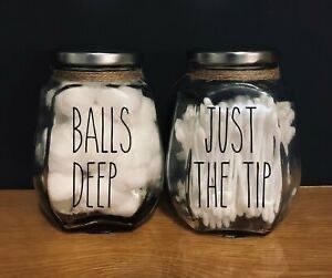 two glass jars with metal lids and twine around the necks are sitting on a wooden surface in front of a dark background. the jar on the left is labeled "balls deep" and filled with cotton balls. the jar on the right is labeled "just the tip" and filled with qtips. the labels are written in a bold, sansserif font.