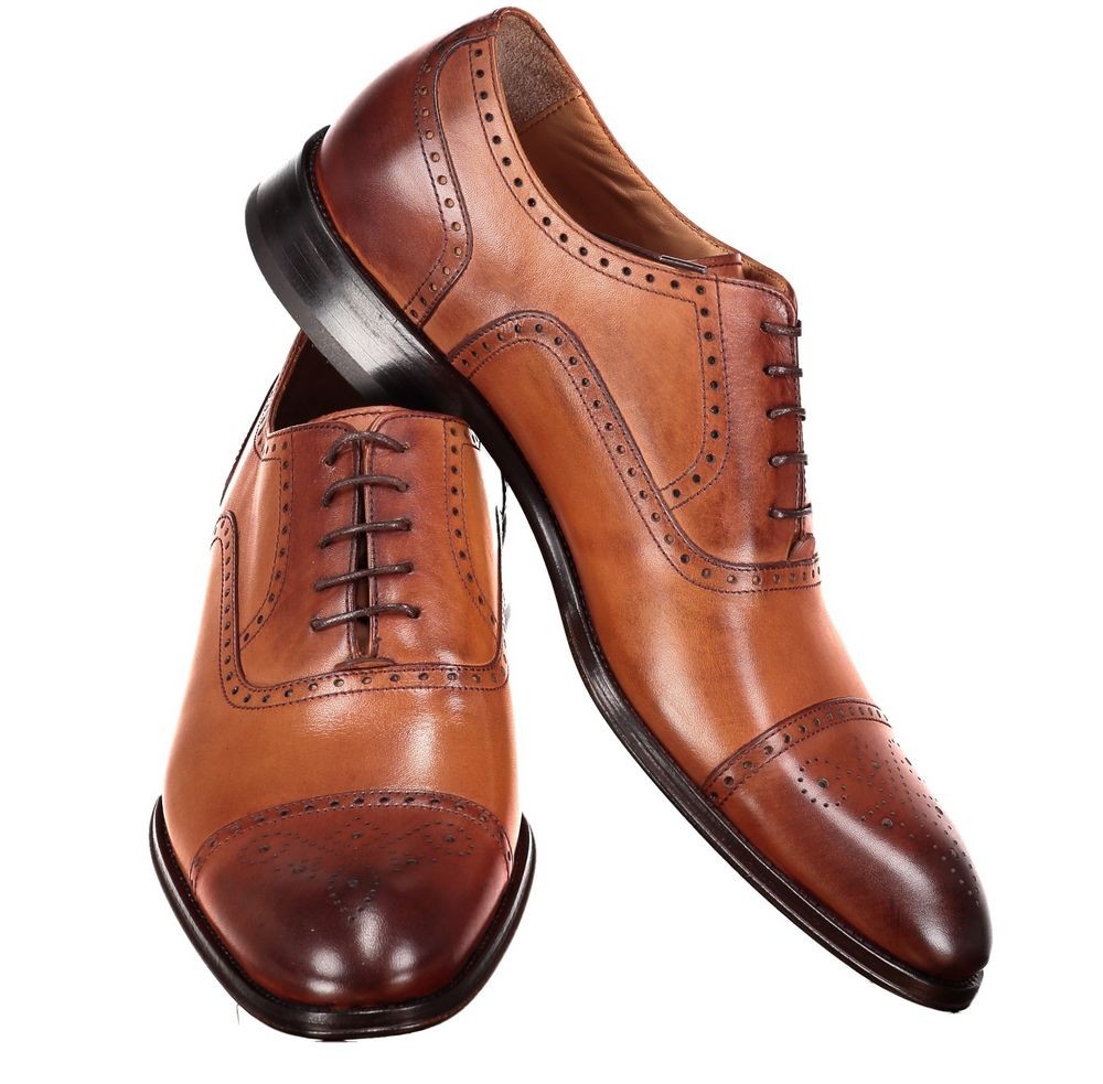 the image showcases a pair of men's brown leather brogue oxford shoes set against a clean white background. the shoes are positioned with one upright and the other leaning against it, offering a clear view of their design and craftsmanship. the warm brown leather, intricate broguing details, and classic oxford silhouette exude an air of sophistication and elegance.