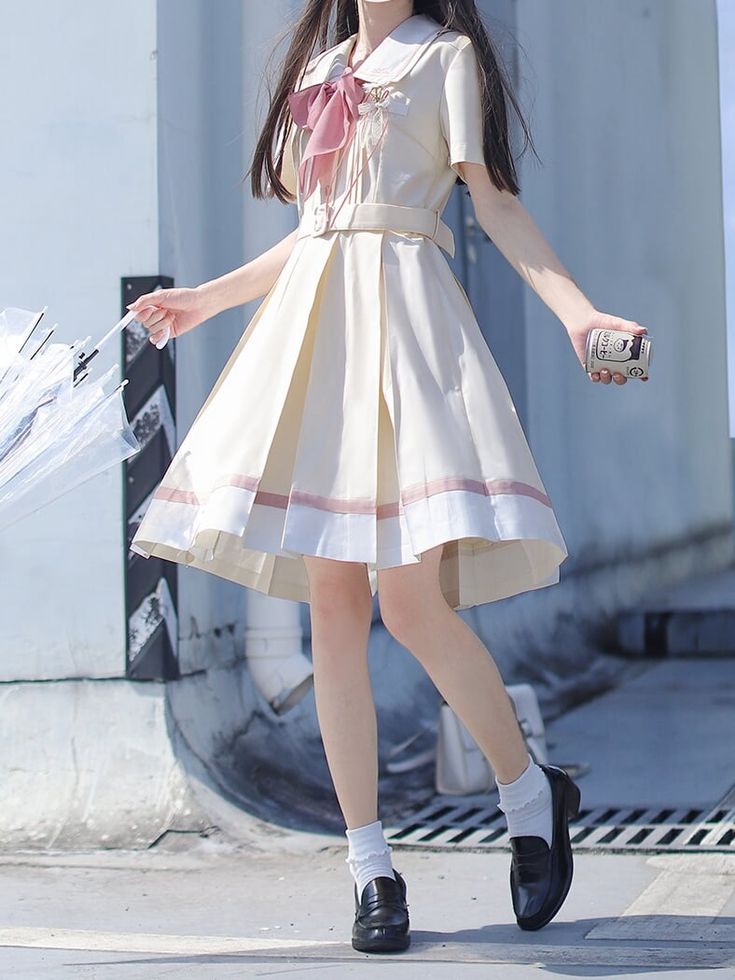 a young woman is standing on a sidewalk, wearing a creamcolored lolitastyle dress with a pink bow. she is holding a transparent umbrella in her left hand and a canned drink in her right hand. she is wearing black leather mary jane shoes with white ankle socks. the image is taken from an eyelevel perspective and the lighting is natural and sunny.