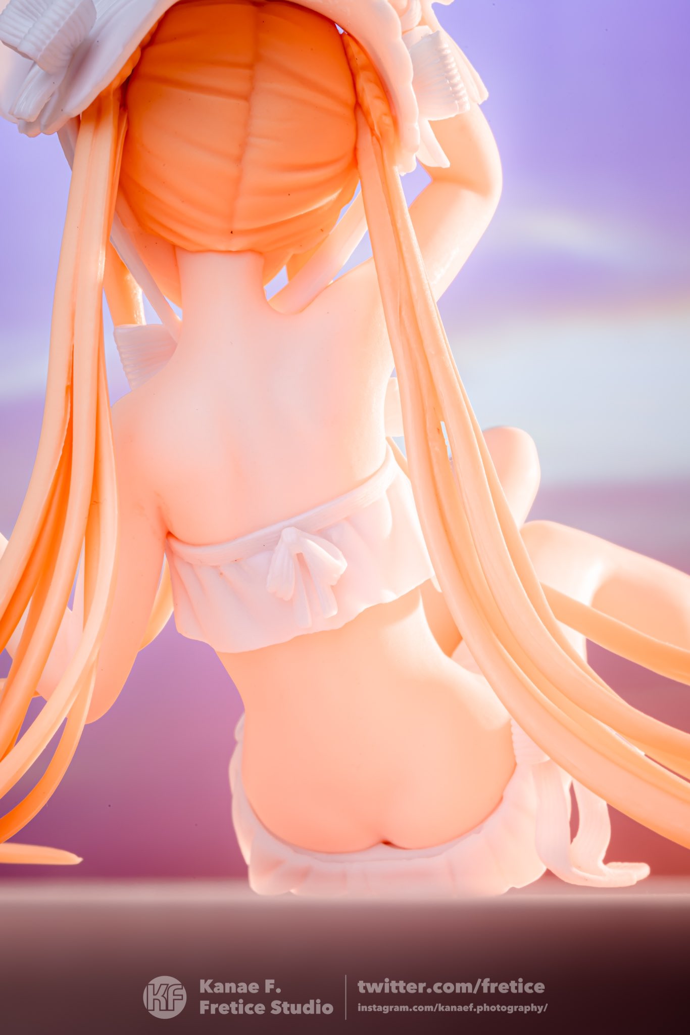 this is a back view closeup shot of an anime figurine, a female character with long blonde hair. she is wearing a white hat and a white twopiece swimsuit.  the figurine is posed as if sitting or relaxing, with her long hair flowing down her back. the background is a soft purple and pink gradient, suggesting a beach or sunset theme. the overall style is cute and kawaii. the photo is professionally taken, emphasizing the detail and quality of the figurine.  the watermark indicates the photographer and studio involved (kanae f., fretice studio).