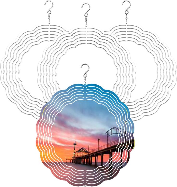 the image shows four round, metal wind spinners hanging. three are plain silver and one has an image of a pier at sunset printed on it. the spinners are hanging from hooks and are visible against a white background. the pier has an arched gateway. the sky is red and pink.
