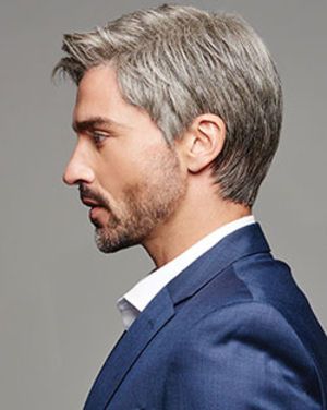 a closeup side profile portrait of a man with a stylish salt and pepper hairstyle, showcasing a popular men's haircut. he is wearing a blue suit jacket and a white shirt. the background is a neutral gray, and the image appears to be professionally lit.