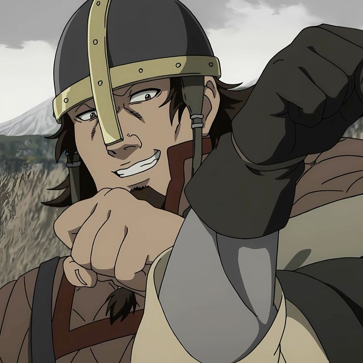 the image shows a man in viking warrior attire. he wears a helmet with metal accents and a brown tunic. he is looking towards the left of the image and has a smirk on his face. his right hand is raised, as if he is in the middle of a fight. he is set against a mountainous backdrop.