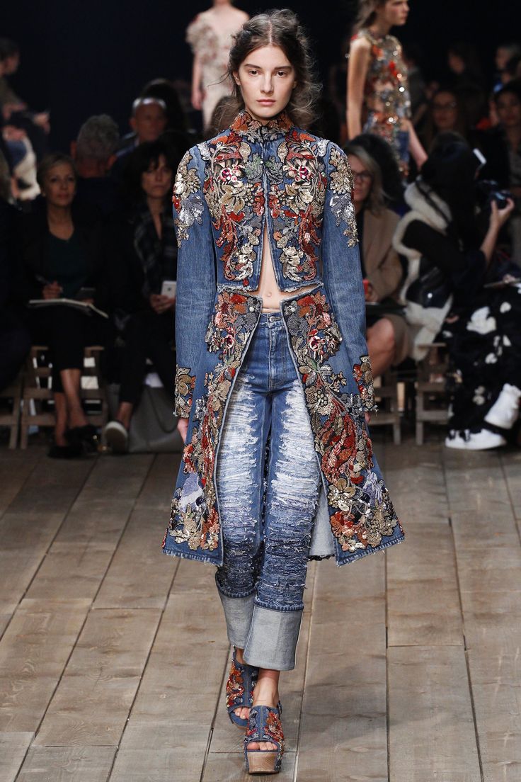 a model walks the runway in a denim jacket and jeans embroidered with floral patterns,  she's paired it with a pair of chunky heeled boots.