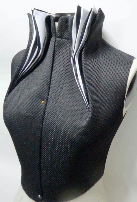 a black mesh bodice on a mannequin with a high, architecturally structured collar lined with white fabric. the design showcases advanced tailoring and garment construction. a pin is visible on the bodice indicating potential alterations or design elements in progress.