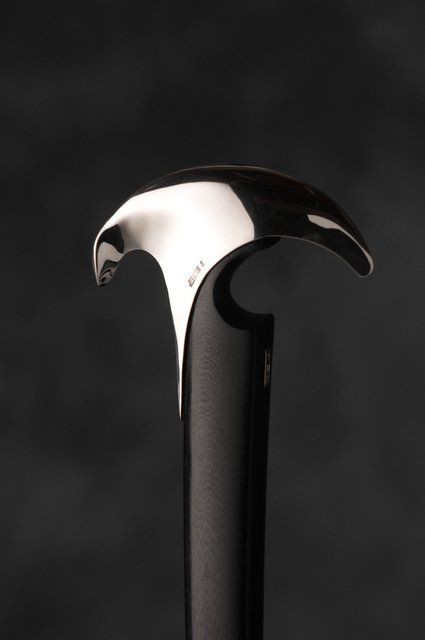a closeup of a walking stick with a silver handle. the handle is shaped like a bird's head, and the shaft is black and wooden. the stick is elegant and stylish. it is likely made of expensive materials, and would be considered a luxury item.