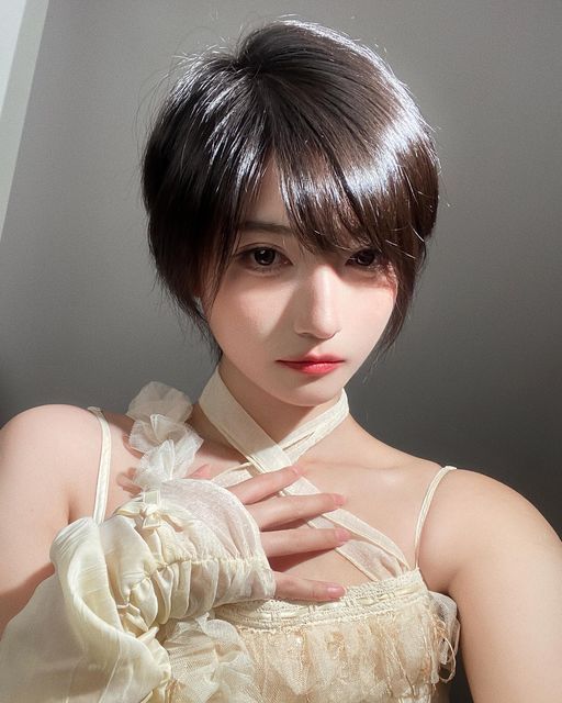 a young asian woman with short, dark hair and bangs looks directly at the camera with a delicate smile. she's wearing a sweet and simple white lace dress that has delicate straps.