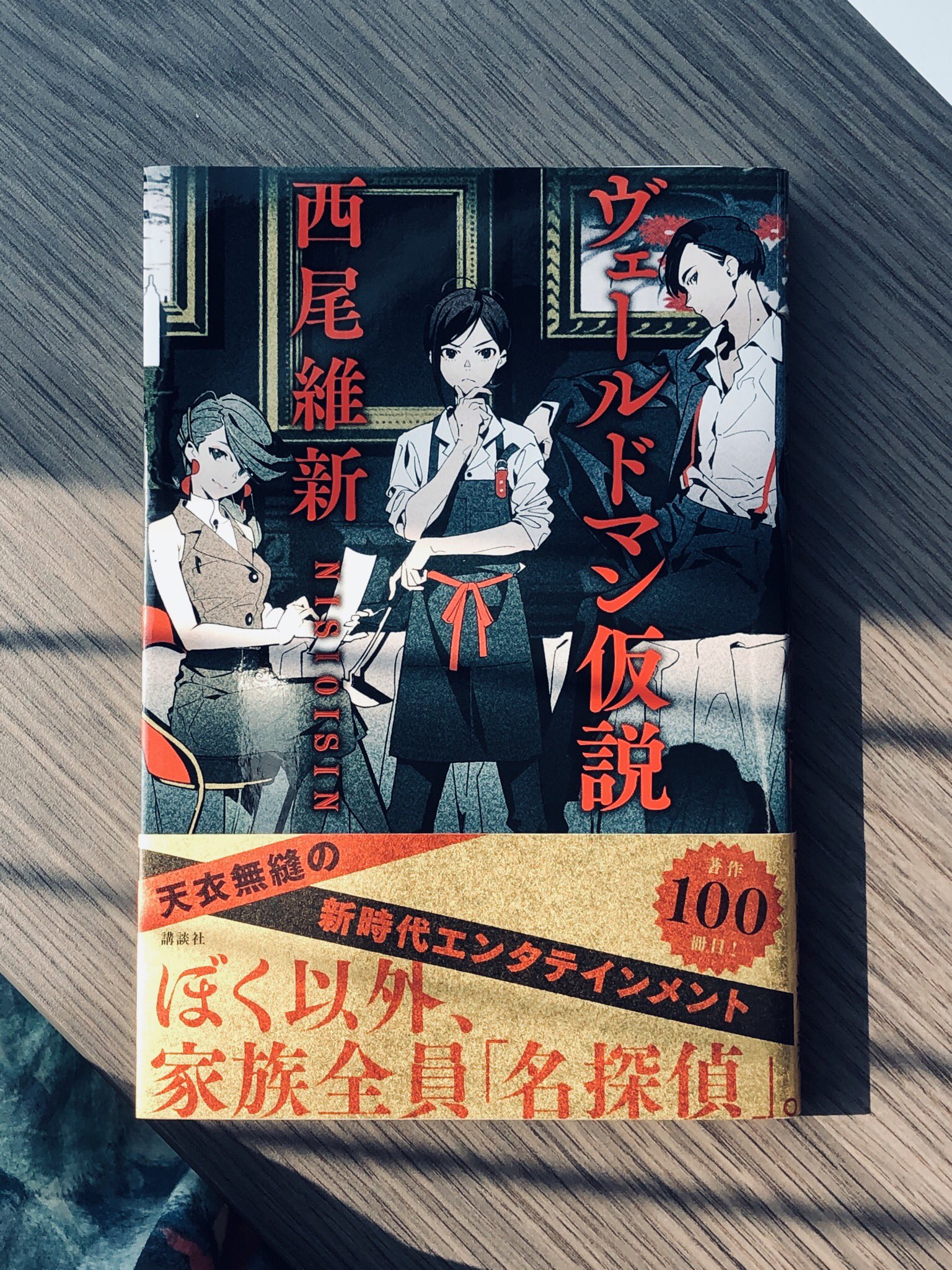 the image shows a japanese novel titled "ウレッドマン仮説" (uredoman kasetsu) by author "西尾維新" (nisio isin). the cover features four animestyle characters, three male and one female, in a room. the promotional text on the cover suggests a mystery theme, with the phrase "家族全員「名探偵」" (my entire family are "great detectives"). the overall design has a sleek, modern aesthetic, with a black, white, and red color scheme. the book appears to be a new release, as indicated by the "100" sticker.