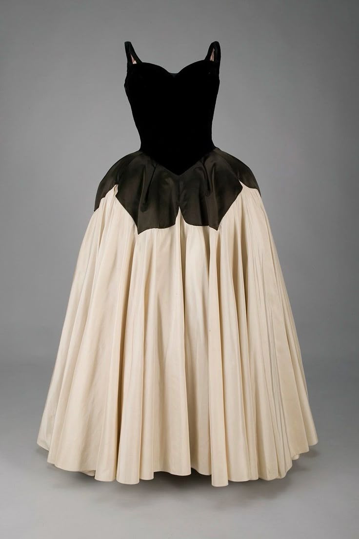 a vintage ball gown is showcased, featuring a black, fitted bodice with thin straps and a sweetheart neckline. the skirt is a full, ivory color that flares out dramatically from the waist. a decorative black fabric detail separates the bodice and skirt. the dress is displayed on a mannequin against a neutral grey background.