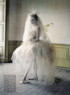 a young woman wearing a white tulle dress and veil, with ghostly pale makeup, looks ethereal and angelic in this studio portrait. the dress is voluminous and flowing, creating a sense of fantasy and magic. her pose and expression are delicate and ethereal, conveying a sense of otherworldliness.  the lighting and setting contribute to the overall ethereal mood of the image.