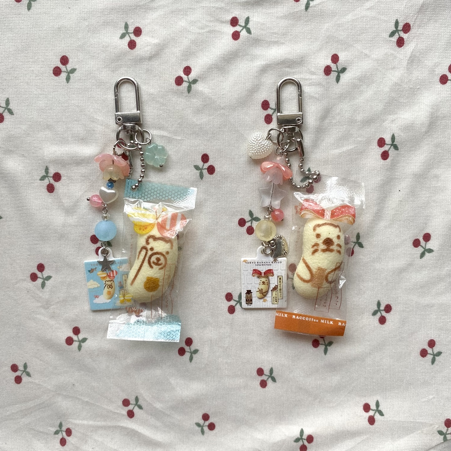 two handmade keychains with different cartoon animal charms are on a cherryprint background. the charms appear to be handmade from felt and packaged in small plastic bags. the keychains have beads and other small decorative elements attached to them.