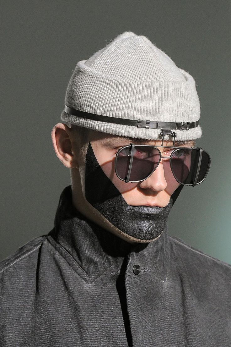 a man in a gray beanie and black sunglasses is posing for a photo. he is wearing a black denim jacket. the image is in a studio setting.