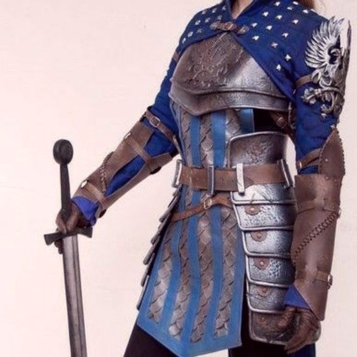 he image shows a woman cosplaying as a female knight in elaborate medieval fantasy armor. the armor is predominantly silver metal with blue leather accents, creating a striking visual effect.  the armor includes a breastplate, pauldrons, gauntlets, and a segmented skirtlike lower section.  a brown leather belt holds the armor together. the knight is holding a short sword and wears a blue tunic under the armor. the level of detail in the costume is impressive, suggesting highquality craftsmanship. the background is a simple, lightcolored backdrop that keeps the focus entirely on the impressive costume.