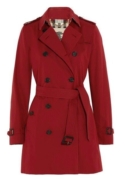 a red doublebreasted trench coat with a belt is displayed on a white background. the coat has dark buttons and a classic design. the inside lining is visible at the collar, showing a patterned fabric.
