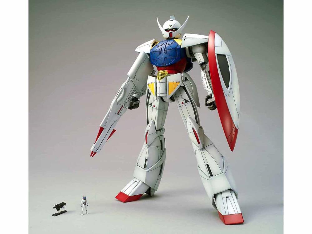 a white, red, blue, and yellow gundam model kit stands tall, its left arm extended forward as if ready to fire its weapon. a smaller action figure stands at its feet for scale, emphasizing the impressive size of the model. the background is a neutral gray, drawing all attention to the meticulously detailed gundam. the soft lighting enhances the smooth surfaces and intricate details of the model.  this image perfectly captures the allure of gunpla building, showcasing the craftsmanship and artistry involved in the hobby.