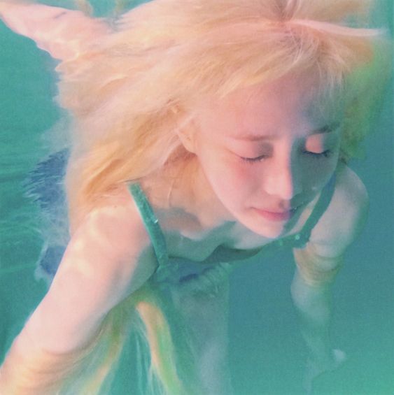 a young woman with blonde hair swims underwater in a turquoise pool. the picture is taken from above, showing the woman's face and upper body submerged.  her eyes are closed, giving a peaceful expression, and her hair flows around her head. the lighting is soft and natural, creating a dreamy atmosphere.