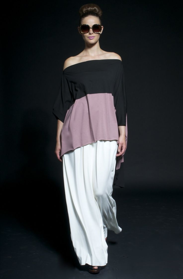 a female model wearing a black and pink shirt with white pants, poses on the runway with black background.