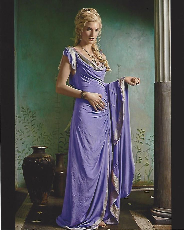 the image is a portrait of a woman dressed in a flowing, purple, grecianstyle gown. her blonde hair is styled in an updo. she is wearing gold jewelry including a necklace and bracelet. the setting appears to be a historically styled room with painted walls featuring a leafy motif and an antiquelooking vase, suggesting an ancient roman or greek setting. the overall impression is one of elegance and historical drama. the woman's pose and expression are calm and sophisticated. the lighting and color palette create a dramatic mood.
