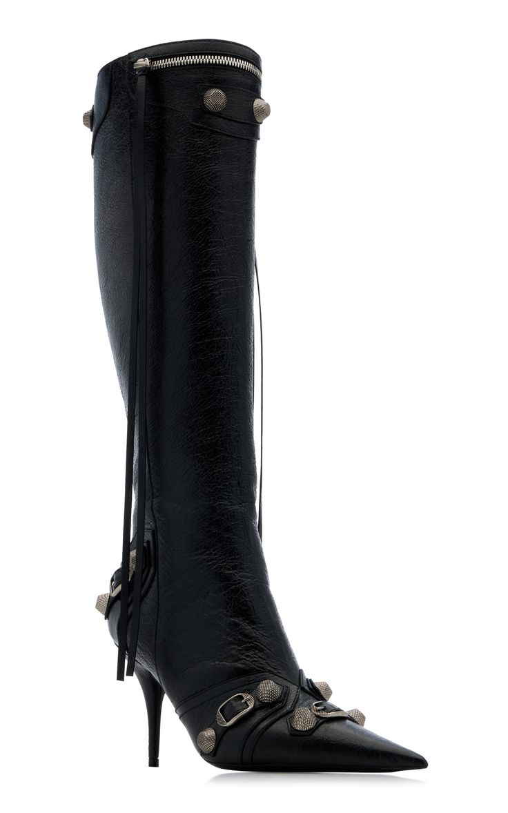a pair of black leather balmain kneehigh boots with pointed toes are shown against a white background. the boots have silvertoned studs and buckles as details, along with a fringe detail on the inside. the boots feature a zipper closure and are styled with high heels.
