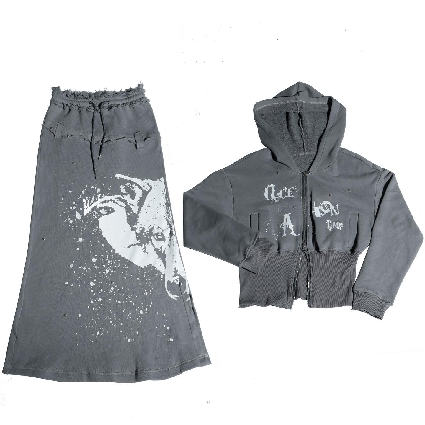 he image shows a twopiece outfit for women. the outfit consists of a long grey skirt and a cropped grey hoodie. both pieces are made of a soft, comfortable material and have a distressed look with white graphic print. the skirt features a wolf graphic print and a drawstring waist. the hoodie has a zipup front, a hood and text printed on the front. the overall style of the outfit is casual and trendy.
