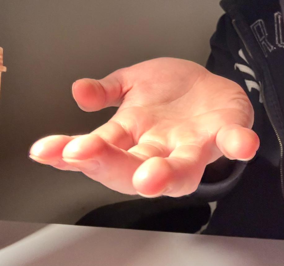 the image shows a hand reaching out with an open palm. the hand is positioned in the foreground with the fingers outstretched. the skin tone is light with warm undertones, and the lighting is soft and natural, creating a gentle shadow underneath the hand. the background is blurred and mostly out of focus, hinting at an indoor setting. the overall impression is of a gesture of offering or receiving.