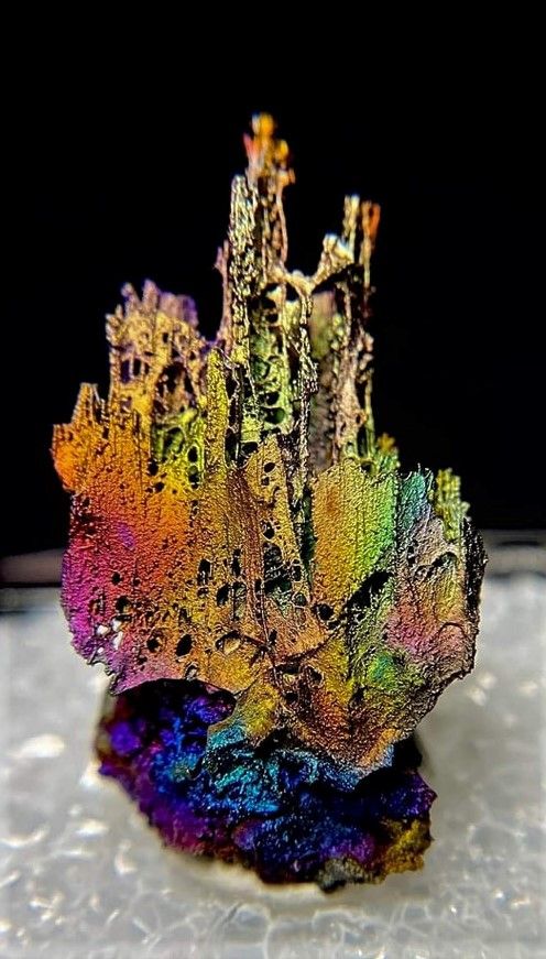 a closeup shot of a mineral crystal with an iridescent surface. the mineral is a beautiful and colorful, displaying a rainbow of colors. the crystal is sitting on a white background.  the mineral's intricate details are highlighted by the macro photography. the image showcases the natural beauty of the mineral.
